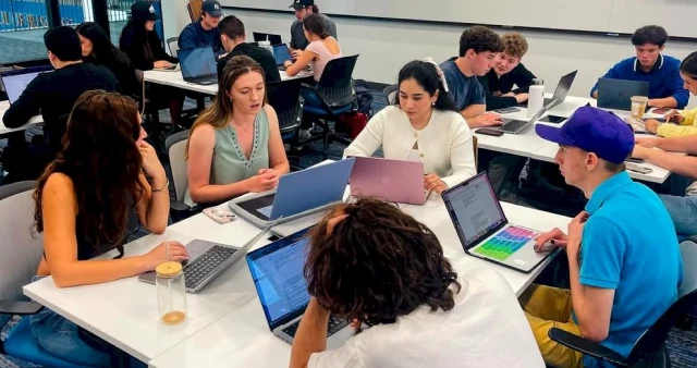 Group of students sitting at a round table with notebooks, discussing together